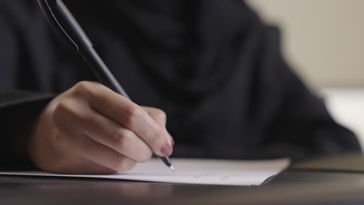 كتابة التقرير اليومي الخاص بالعمل , امرأة عربية خليجية سعودية ترتدي العباءة السوداء تستخدم القلم الجاف في تسجيل الملاحظات ,