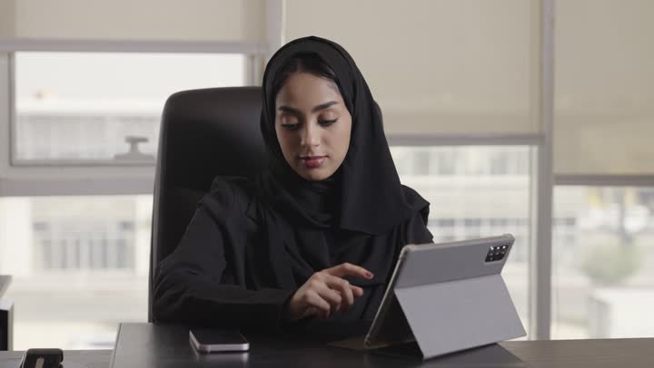 استخدام الجهاز اللوحي في الاعمال الهندسية لتوفير الوقت و المجهود , امرأة عربية خليجية سعودية ترتدي العباءة السوداء تقوم باجراء المحادثات الهاتفية الخاصة بالعمل , الجلوس على مكتب الشركة