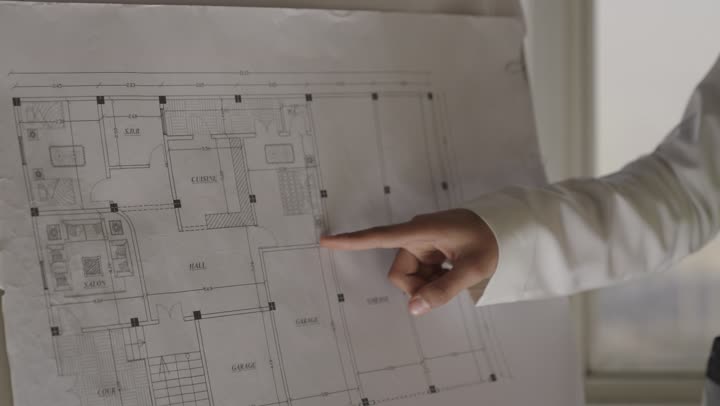 الاشارة باصبع السبابة الي الرسومات الهندسية المعلقة على طاولة العرض , مهندس عربي خليجي سعودي يرتدي السترة الواقية العاكسة للضوء , الحفاظ على تعليمات السلامة و الامان , رفع الابهام علامة على الموافقة و الاعجاب بالتخطيط الهندسي