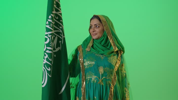 يوم بدينا 1727 م، ذكرى تأسيس الدولة السعودية الأولى 22 فبراير، ارتداء زي المنطقة الوسطى في المناسبات الشعبية والوطنية,  الاعتزاز بإنجازات الوطن، شعار الهوية الوطنية وراية الإسلام والتوحيد، بورتريه لامراه عربيه خليجيه سعوديه كبيرة بالسن ترتدي البرقع والشيلة تحمل بيدها علم التأسيس, تنظر بايماءات الفخر، كروما، خلفية خضراء