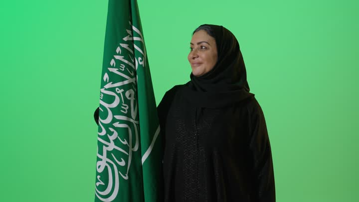 بورتريه لامراه عربيه خليجيه سعوديه كبيرة بالسن ترتدي العباءة السوداء تحمل بيدها علم التأسيس, تنظر بايماءات الفخر، شعار الهوية الوطنية وراية الإسلام والتوحيد، ذكرى تأسيس الدولة السعودية الأولى 22 فبراير، الاعتزاز بإنجازات الوطن، كروما، خلفية خضراء