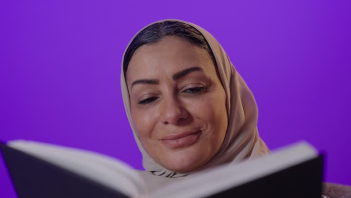 الشعور بالراحة والطمأنينة, قراءة الروايات والقصص الممتعة،  بورتريه لإمرأة كبيرة بالسن عربية خليجية سعودية محجبة ترتدي العباءة تمسك بيدها الكتاب، الاسترخاء والاستمتاع بالأجواء الهادئة، اتباع أسلوب حياة صحي، خلفية بنفسجية