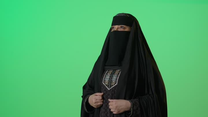 أزياء محجبات عصرية حديثة،  بورتريه لامراه عربيه خليجيه سعوديه منتقبة كبيرة بالسن ترتدي العباءة السوداء تنظر بإيماءات الثقه بالنفس، الاهتمام بالمظهر الخارجي، مفهوم الأنوثة والأناقة والشياكة والنعومة، كروما، خلفية خضراء