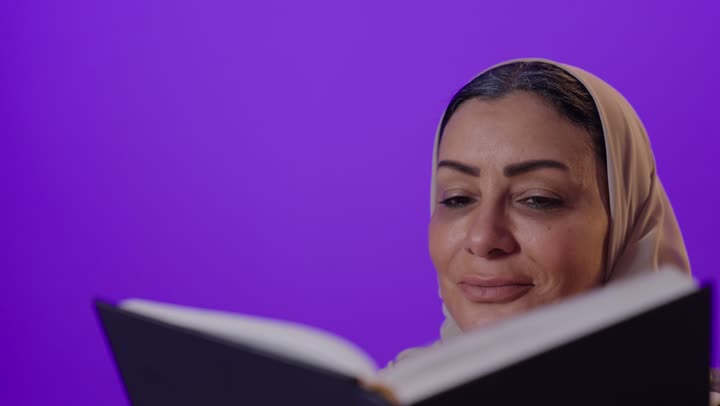 قراءة الروايات والقصص الممتعة،  الشعور بالراحة والطمأنينة, بورتريه لإمرأة كبيرة بالسن عربية خليجية سعودية محجبة ترتدي العباءة تمسك بيدها الكتاب، الاسترخاء والاستمتاع بالأجواء الهادئة، اتباع أسلوب حياة صحي، خلفية بنفسجية