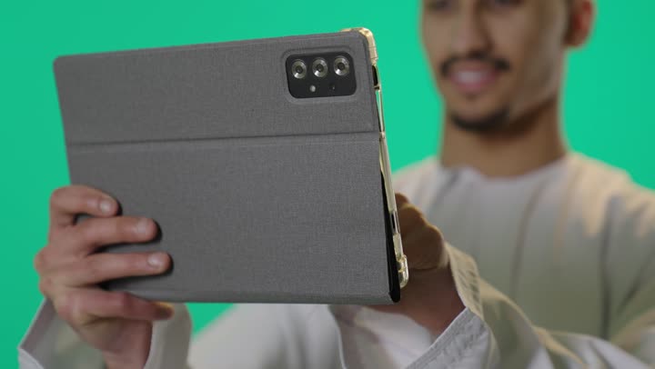 تصفح مواقع التواصل الاجتماعي، استخدام التكنولوجيا المتطورة، بورتريه مقرب لشاب عربي خليجي عماني يرتدي الدشداشة و الكمه يحمل بيده جهاز التابلت اللوحي , الدردشة والتواصل مع الأهل والأصدقاء