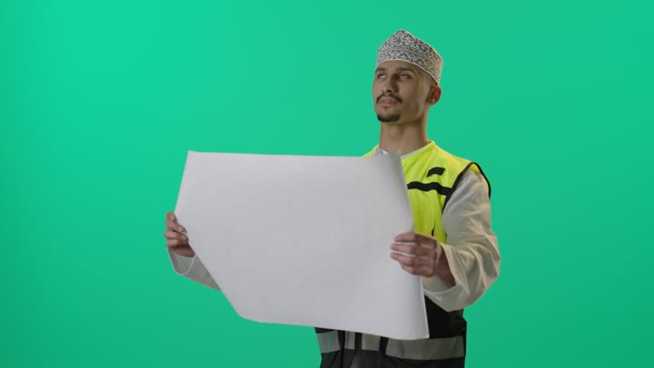 Project plan auditing, a portrait of an Arab Gulf Omani engineer wearing a dishdasha, helmet, and safety vest holding an engineering plan, supervising construction engineering projects, green background.