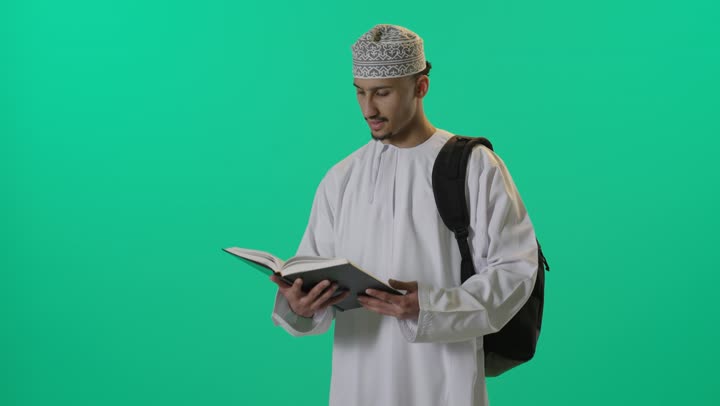 قضاء أوقات الفراغ بالتثقيف والتعلم, الاهتمام بتصفح الكتب المفيدة, بورتريه لطالب عربي خليجي عماني يرتدي الدشداشة والكمه العمانية حقيبة الظهر يمسك بيده كتاب, تنمية مهارات القراءة، خلفية خضراء