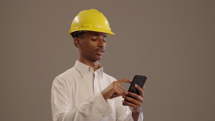 دمج التكنولوجيا الحديثة في الأعمال الهندسية, هواية المطالعة والاستكشاف, التواصل مع الأهل والأصدقاء, بورتريه لطالب جامعي عربى خليجى سعودى اسمر يرتدي الثوب التقليدى و الخوذة يحمل بيده الهاتف المحمول , خلفية بيج