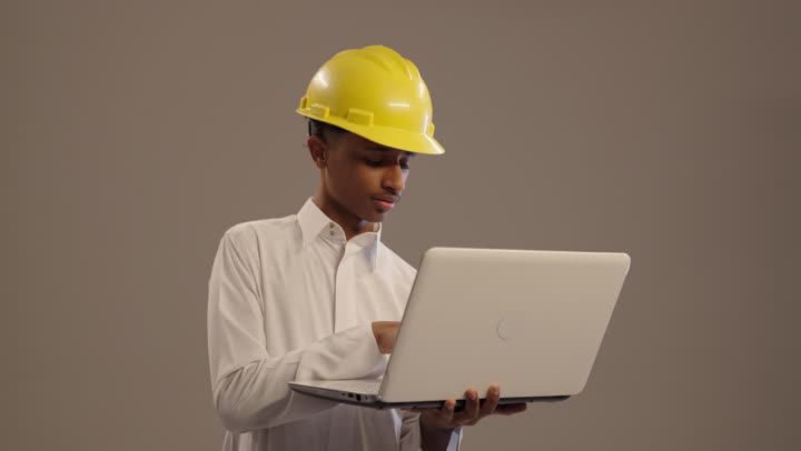 تجريب المهن المستقبلية منذ الصغر, بورتريه لطالب عربي خليجي سعودي يرتدى الثوب التقليدي يضع خوذة صفراء اللون يقوم بالنقر على الحاسوب , دمج التكنولوجيا الحديثة في الأعمال الهندسية, خلفية بيج