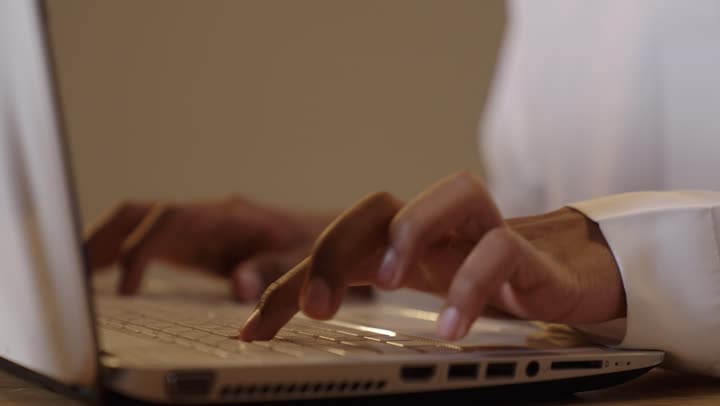 Studying and distance learning, the concept of e-learning, a close-up portrait of the hand of a Saudi Gulf Arab student clicking on the computer, attending classes and solving assignments online, background in beige.