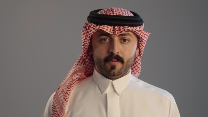 عدم الإعجاب وعدم قبول شيء ما، التقييم السلبي والفشل, بورتريه لرجل عربي خليجي سعودي يرتدي الثوب التقليدي والشماغ,  إيماءات إبهام لأسفل تدل على الرفض والإستياء وعدم الرضا, خلفية رمادية