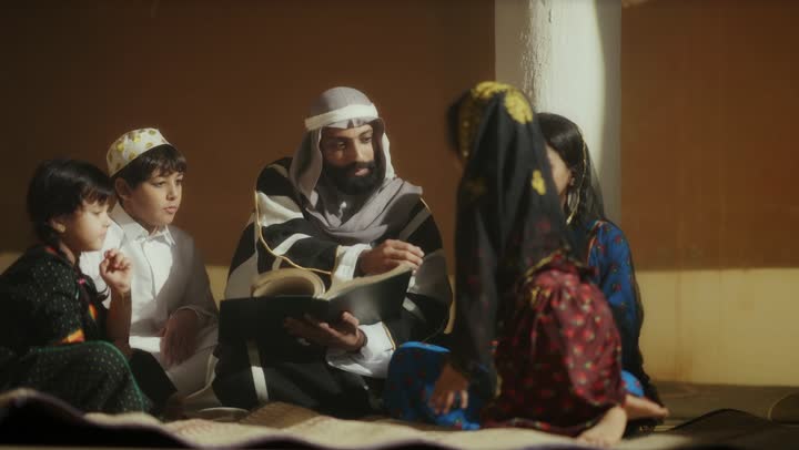 رجل  كبير السن عربي سعودي خليجي يرتدي البشت وعقال يجالس الاطفال ويقرألهم كتاب تاريخي يوم التأسيس, ذكرى تأسيس الدوله السعوديه الاولى على يد  الامام محمد بن سعود, يوم بدينا 22 فبراير 1727م, الفخر بإنجازات الوطن, تحقيق الهويه الوطنيه