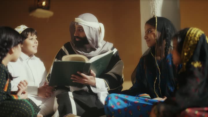 A Saudi Arabian man from the Gulf region, wearing a bisht and agal, sits with a group of children on the anniversary of the founding of the first Saudi state by Imam Muhammad bin Saud, February 22, 1727, the day we began, expressing pride in the nation's achievements and the realization of national identity.