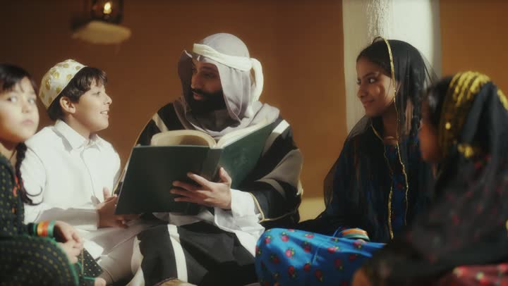 رجل عربي سعودي خليجي يرتدي البشت وعقال يوم التأسيس يجلس مع مجموعه من الاطفال ويقرأ لهم كتاب تاريخي قديم, ذكرى تأسيس الدوله السعوديه الاولى على يد  الامام محمد بن سعود, يوم بدينا 22 فبراير 1727م, الفخر بإنجازات الوطن, تحقيق الهويه الوطنيه