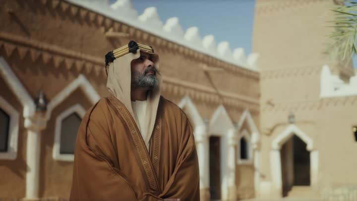 رجل  كبير السن عربي سعودي خليجي يرتدي البشت وعقال يوم التأسيس  يقف في مبنى طيني شعبي قديم النظر لشيء ما في الأعلى, ذكرى تأسيس الدوله السعوديه الاولى على يد  الامام محمد بن سعود, يوم بدينا 22 فبراير 1727م, الفخر بإنجازات الوطن, تحقيق الهويه الوطنيه