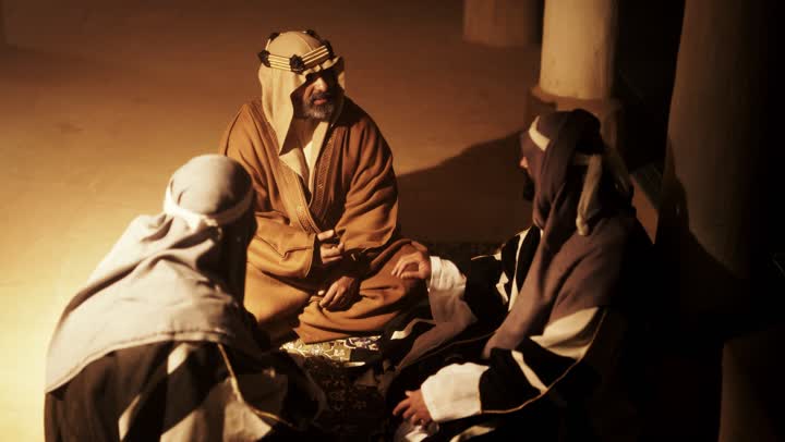 رجل كبير السن عربي سعودي خليجي يرتدي البشت وعقال يوم التأسيس يجلس مع رجلين داخل مبنى طيني, ذكرى تأسيس الدوله السعوديه الاولى على يد الامام محمد بن سعود, يوم بدينا 22 فبراير 1727م,  العمق التاريخي والحضاري للمملكة، ارتداء الأزياء التقليدية تعكس التراث