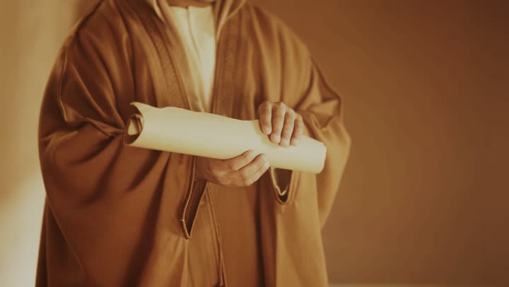 رجل كبير السن عربي سعودي خليجي يرتدي البشت وعقال يوم التأسيس يفتح لفافة ورقية داخل مبنى طيني, ذكرى تأسيس الدوله السعوديه الاولى على يد الامام محمد بن سعود, يوم بدينا 22 فبراير 1727م,  العمق التاريخي والحضاري للمملكة، ارتداء الأزياء التقليدية تعكس التراث