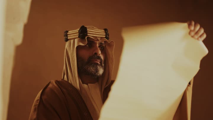 رجل كبير السن عربي سعودي خليجي يرتدي البشت وعقال يوم التأسيس يفتح لفافة ورقية داخل مبنى طيني, ذكرى تأسيس الدوله السعوديه الاولى على يد الامام محمد بن سعود, يوم بدينا 22 فبراير 1727م,  العمق التاريخي والحضاري للمملكة، ارتداء الأزياء التقليدية تعكس التراث