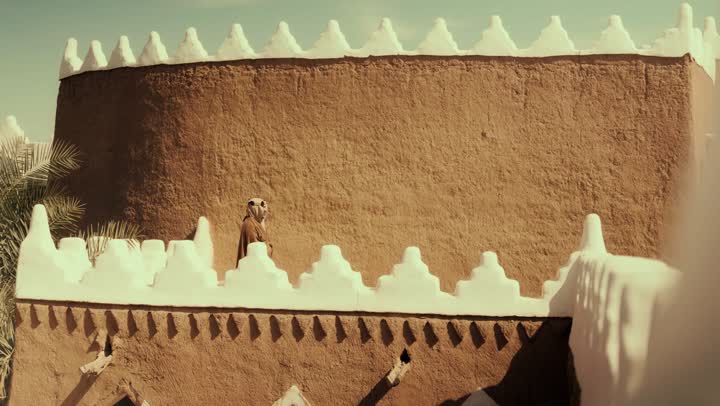 An elderly Arab Saudi Gulf man wearing a bisht and agal stands on a mud building, commemorating the founding of the first Saudi state by Imam Muhammad bin Saud, on the day we began, February 22, 1727. The historical and cultural depth of the Kingdom, the concept of love for the homeland and belonging to it.