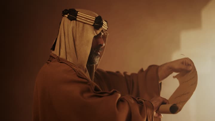 رجل كبير السن عربي سعودي خليجي يرتدي البشت وعقال يوم التأسيس يقرأ مضمون لفافة ورقية داخل مبنى طيني, ذكرى تأسيس الدوله السعوديه الاولى على يد الامام محمد بن سعود, يوم بدينا 22 فبراير 1727م,  العمق التاريخي والحضاري للمملكة، ارتداء الأزياء التقليدية تعكس التراث