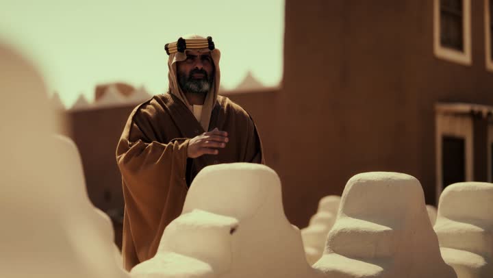 An elderly Arab Saudi Gulf man wearing a bisht and agal stands on a mud building, commemorating the founding of the first Saudi state by Imam Muhammad bin Saud, on the day we began, February 22, 1727. The historical and cultural depth of the Kingdom, the concept of love for the homeland and belonging to it.