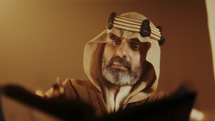 On the day we began, February 22, 1727, the anniversary of the establishment of the first Saudi state by Imam Muhammad bin Saud, wearing traditional attire, a close-up shot of an elderly Arab Saudi Gulf man wearing a bisht and agal on the Foundation Day writing a message on an old paper scroll, the historical and cultural depth of the Kingdom.