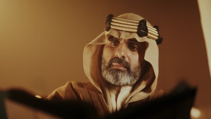 The anniversary of the establishment of the first Saudi state by Imam Muhammad bin Saud, wearing traditional attire, a close-up shot of an elderly Arab Saudi Gulf man wearing a bisht and agal on the founding day writing a message on an old paper scroll, the day we began, February 22, 1727 AD, the historical and cultural depth of the Kingdom.