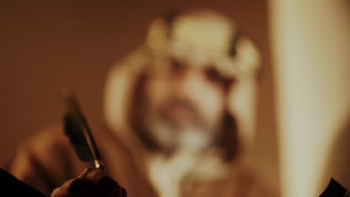 On the day we began, February 22, 1727, the anniversary of the establishment of the first Saudi state by Imam Muhammad bin Saud, wearing traditional attire, a close-up shot of an elderly Arab Saudi Gulf man wearing a bisht and agal on the Foundation Day writing a message on an old paper scroll, the historical and cultural depth of the Kingdom.