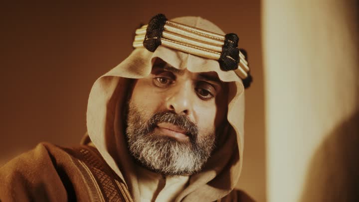 The anniversary of the establishment of the first Saudi state by Imam Muhammad bin Saud, wearing traditional attire, a close-up shot of an elderly Arab Saudi Gulf man wearing a bisht and agal on the founding day writing a message on an old paper scroll, the day we began, February 22, 1727 AD, the historical and cultural depth of the Kingdom.