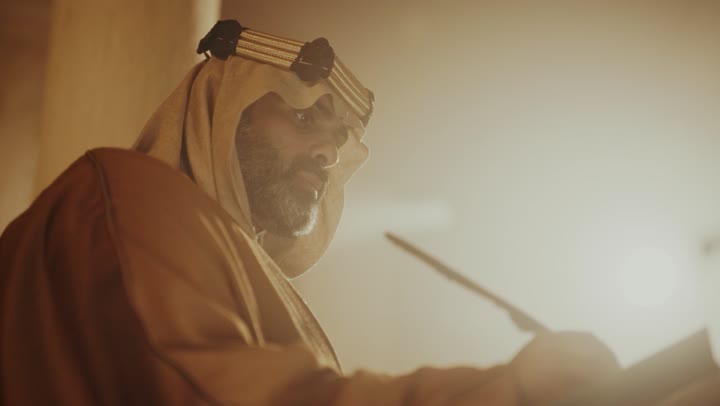 The anniversary of the establishment of the first Saudi state by Imam Muhammad bin Saud, wearing traditional attire, a close-up shot of an elderly Arab Saudi Gulf man wearing a bisht and agal on the founding day writing a message on an old paper scroll, the day we began, February 22, 1727 AD, the historical and cultural depth of the Kingdom.