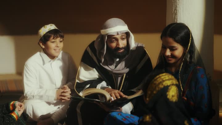 A story for the children, sitting in one of the traditional clay houses, on the day we began in 1727 AD, the love among family members, the anniversary of the founding of the first Saudi state on February 22, an Arab Gulf Saudi man sitting with his children wearing traditional costumes during national holidays.
