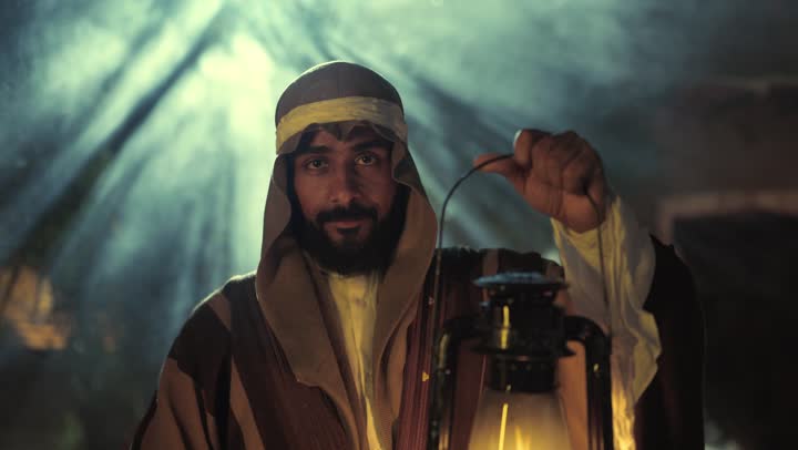The anniversary of the establishment of the first Saudi state is on February 22, showing love and loyalty to the state and the homeland. An Arab Gulf Saudi man wearing traditional folk attire holds a lit lantern in his hand, a source of pride and honor for the national identity. It is the day we began in 1727 AD, a national holiday and occasion, with a popular neighborhood and traditional clay houses.