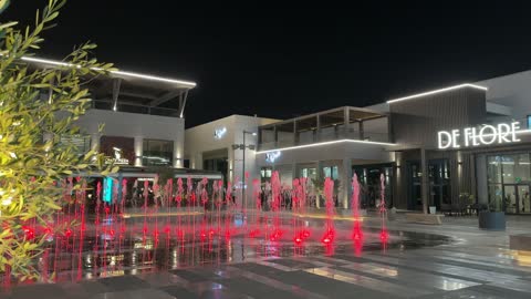 نوافير راقصة مضاءة باللون الأحمر في ساحة تجارية ليلاً