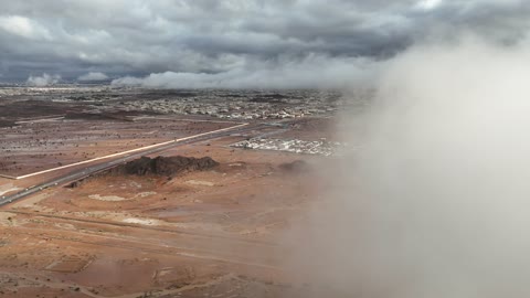 لقطة جوية للسحب والضباب فوق مدينة صحراوية وطريق سريع