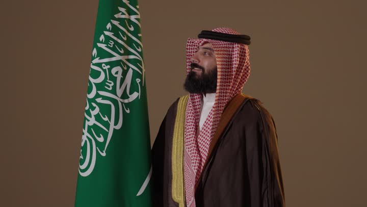 رجل سعودي بالبشت التقليدي مع العلم في يوم التأسيس