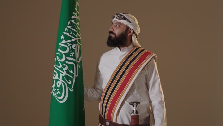 رجل سعودي بزي يوم التأسيس مع العلم السعودي في الاستوديو