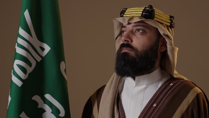 رجل سعودي بزي يوم التأسيس التقليدي مع العلم الوطني