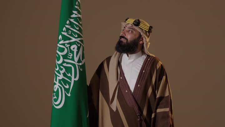 رجل سعودي يرتدي ملابس يوم التأسيس التقليدية مع العلم
