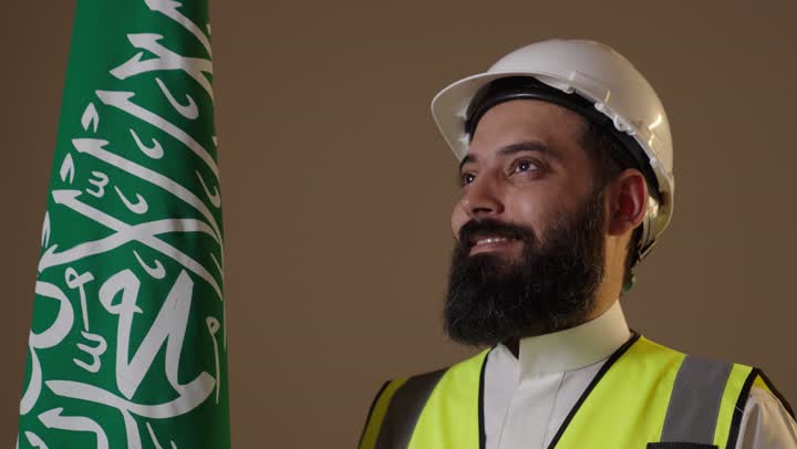 مهندس سعودي يقف بجانب العلم بملابس السلامة