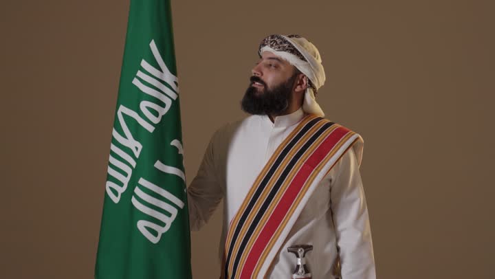 رجل سعودي بزي يوم التأسيس مع العلم الوطني