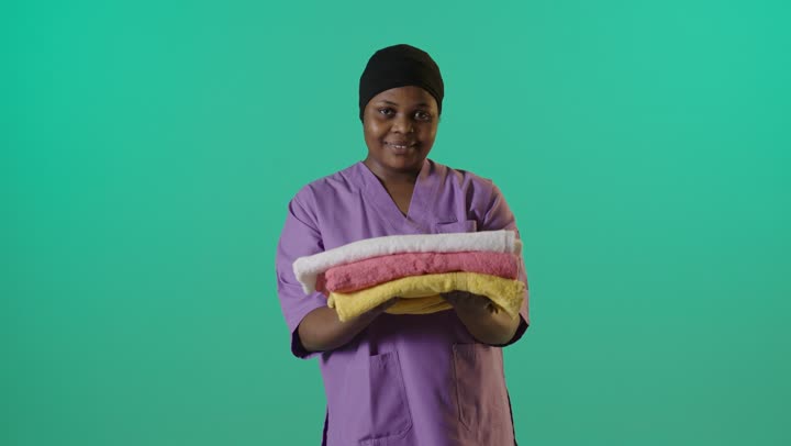 عاملة أفريقية تحمل مناشف مطوية خلفية خضراء