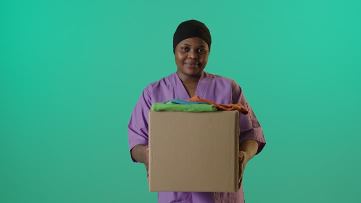 عاملة تحمل صندوق ملابس أمام كروما خضراء
