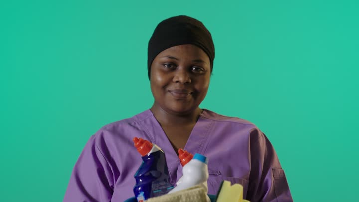 عاملة نظافة أفريقية تحمل دلو منظفات خلفية خضراء