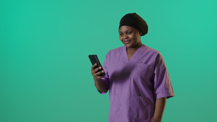 ممرضة سمراء تستخدم الهاتف الذكي أمام خلفية خضراء