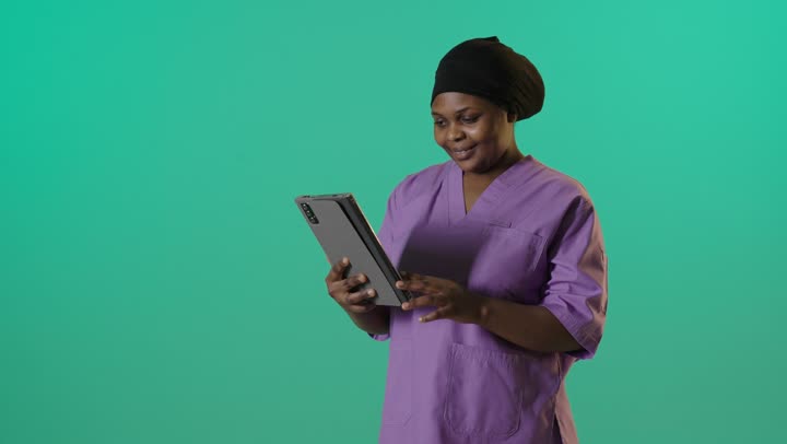 ممرضة أفريقية تستخدم جهاز لوحي رقمي أمام خلفية خضراء
