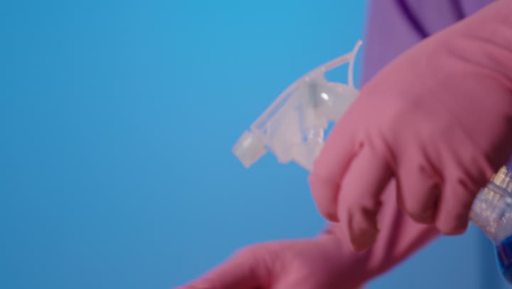 شخص يرش سائل التنظيف بقفازات وردية