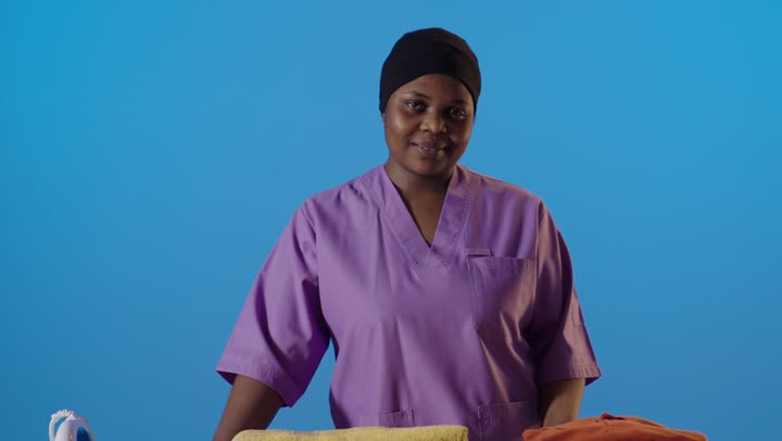 عاملة منزلية أفريقية تكوي الملابس وتشير بالإبهام