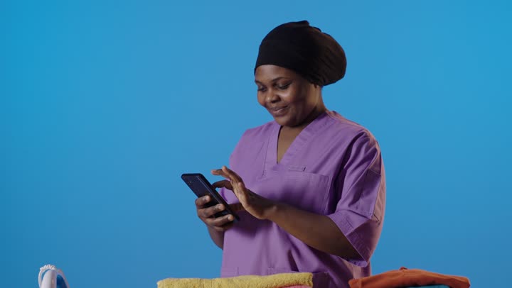خادمة أفريقية تستخدم الهاتف الذكي عند طاولة الكي