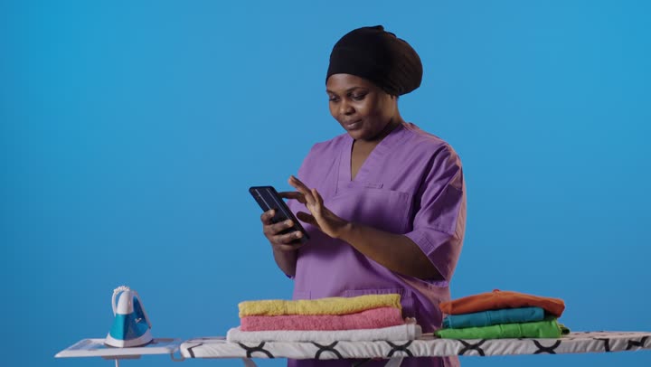 African Domestic Worker Using Smartphone While Ironing