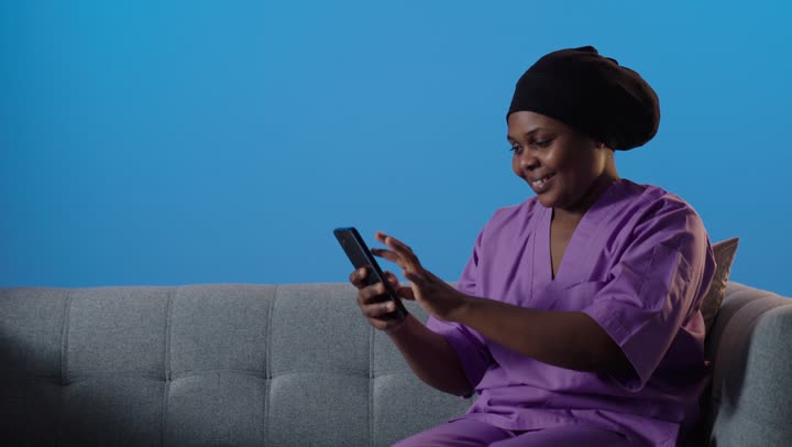ممرضة أفريقية تستخدم الهاتف الذكي أمام خلفية زرقاء